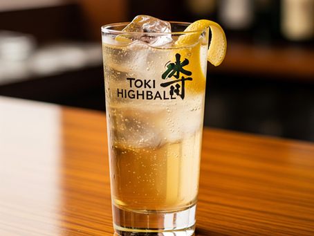 Ein Toki Highball Cocktail in einem hohen Glas mit Eis und Zitronenzeste, auf einer glänzenden Holztheke.