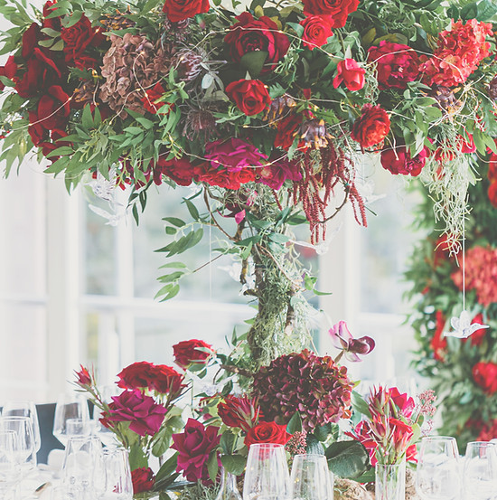Centerpiece aus roten und pinken Blumen auf weiss eingedecktem, runden Hochzeitstisch