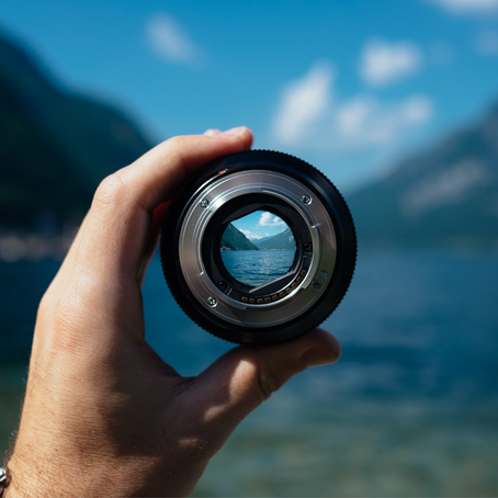 A person's hand holding a lens where you see a river between two mountains with blue skies above.