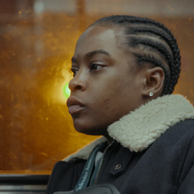 A Black woman with cornrows sits near a window. 