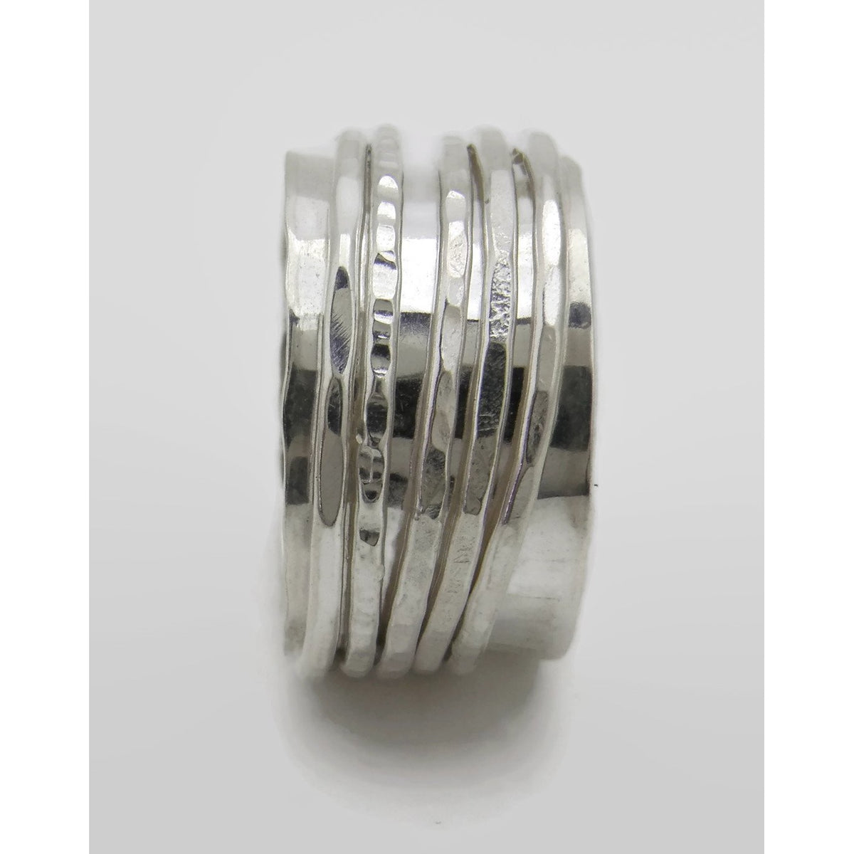 Close-up of a handmade silver spinner ring featuring a wide polished band wrapped with multiple freely moving silver bands in varied hammered and textured finishes.