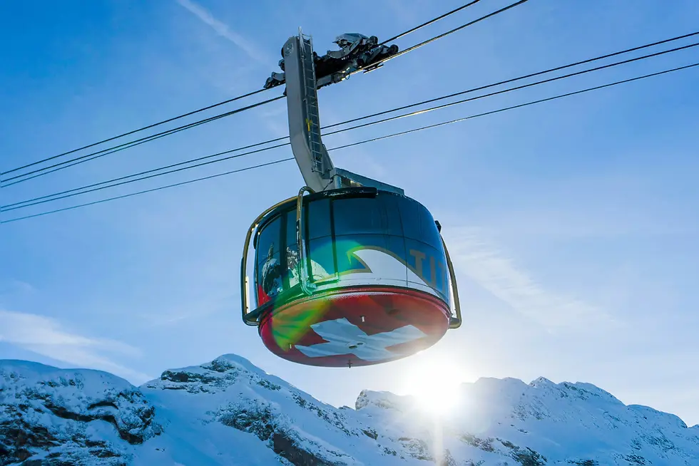 A modern glass cable car ascends past sunlit snowfields with lens flare on the cabin.