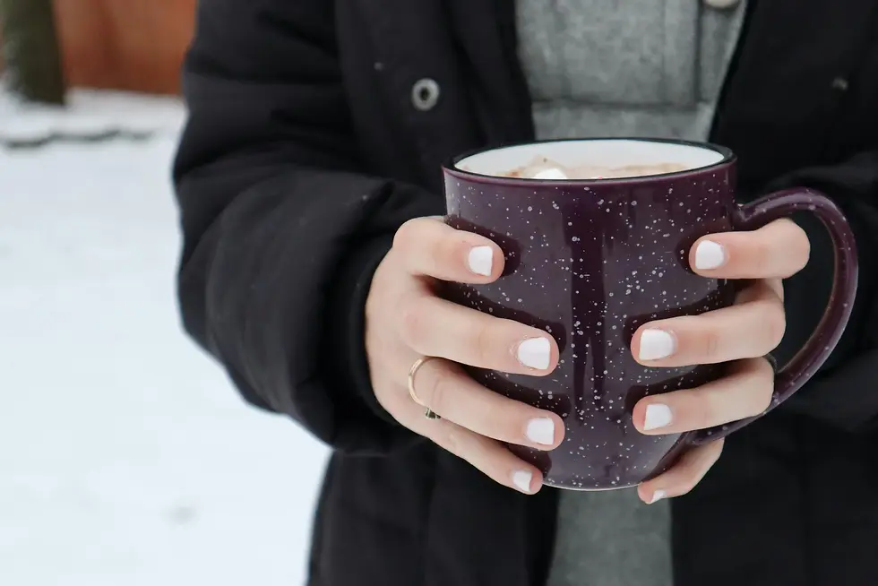 Seseorang memegang erat mug besar berisi cokelat panas di tengah suasana bersalju, menunjukkan bagaimana minuman hangat Swiss menemani momen santai di musim dingin.