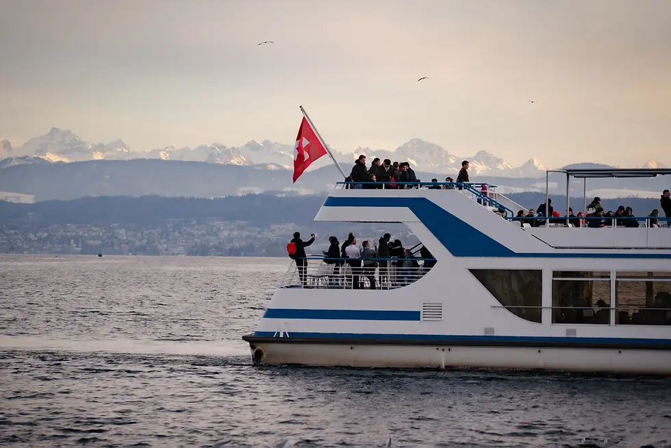 A classic Swiss boat with warm deck lights glides across a calm river at dusk.