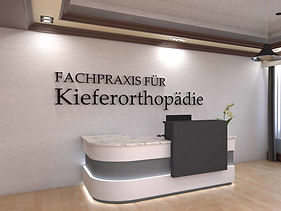 Empfangsbereich einer modernen Zahnarztpraxis mit stilvollem Empfangstresen und Akustik-Wall-Art-Schriftzug 'Fachpraxis für Kieferorthopädie' als schallabsorbierendes Wand-Element – elegante Kombination aus Raumakustik und Praxisdesign