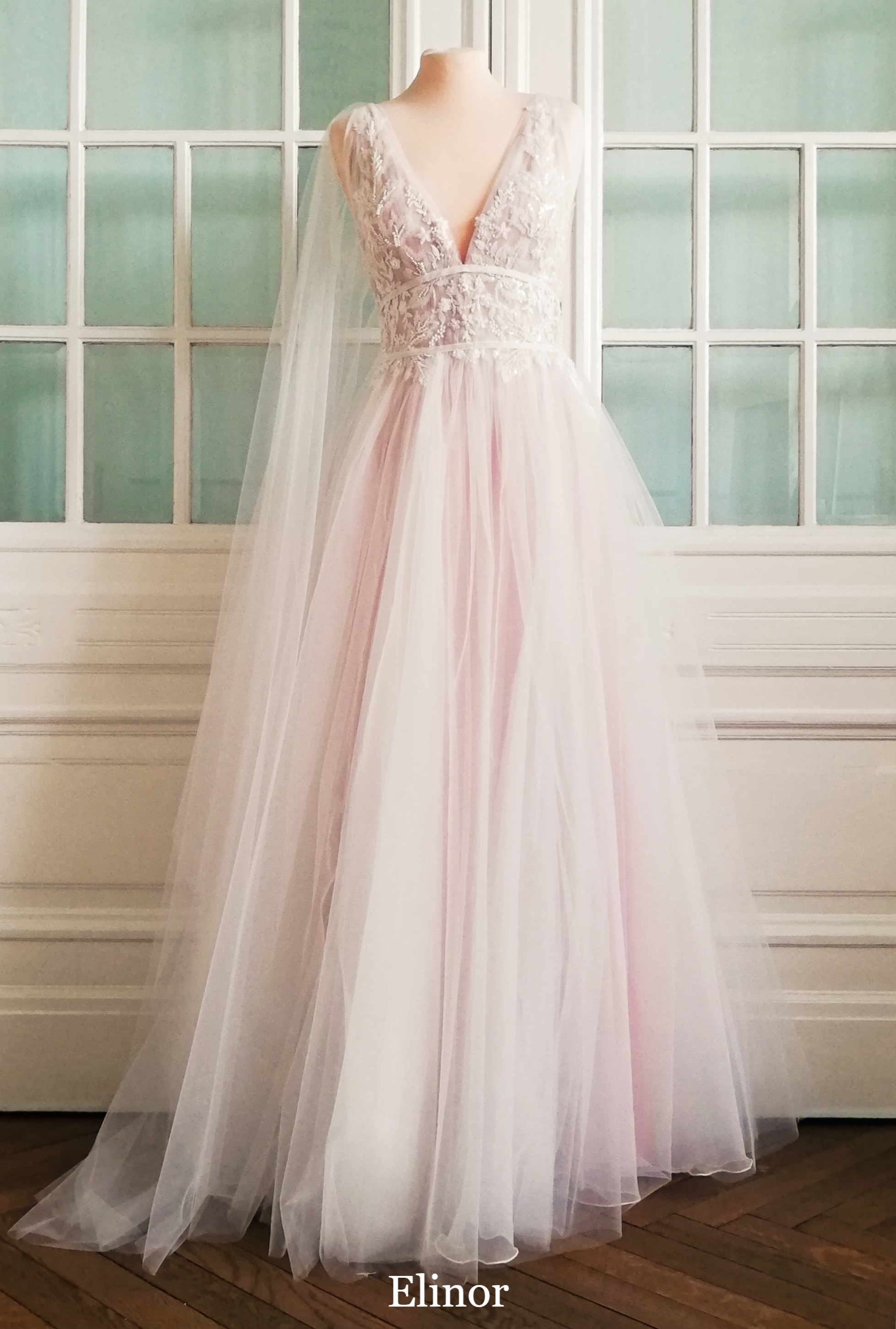 Mehrlagiges Tüllkleid mit tiefem V-Ausschnitt vorne und hinten, Oberteil mit filigraner, milchig-glitzernder Spitze, Taille mit Samtbändern betont, Unterkleid hell pudrig.