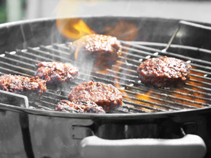 Grilling burgers on a black charcoal grill with flames and smoke rising. The patties are sizzling, creating a warm, outdoor cooking vibe.