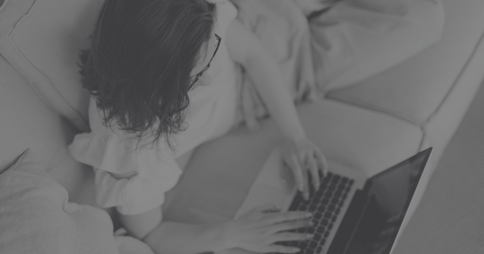 Woman in glasses lying on a couch using a laptop. Soft lighting, relaxed mood. Monochrome tone emphasizes tranquility.
