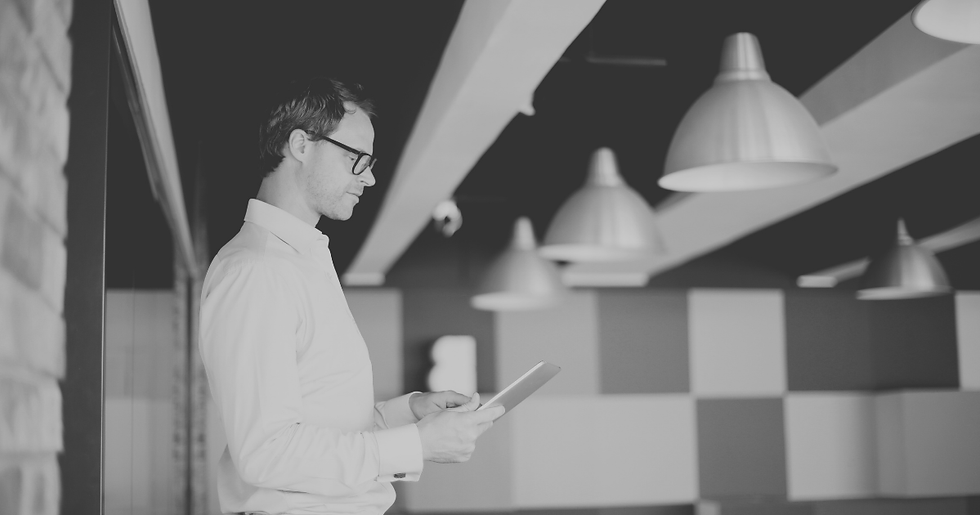 Man in glasses holding a tablet in a modern office with pendant lights and geometric wall panels, calm and focused.