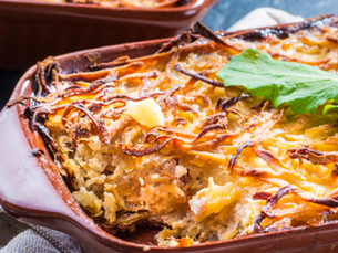 Golden-brown baked dish with crispy top and green garnish in a ceramic dish, set on a cloth against a dark background. Cozy mood.
