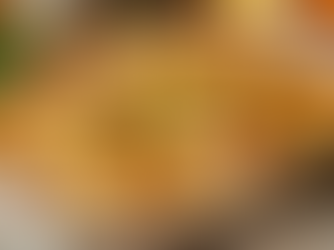 Golden baked dish topped with herbs in a white casserole. Background features a salad, red dish, and wooden table, creating a cozy vibe.