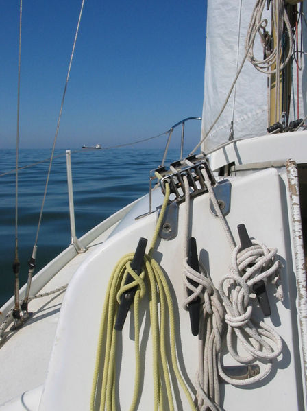 close-up vertical photo from the deck of a sailboat showing rigging lines and cleats, calm blue sea and clear sky, portrait orientation