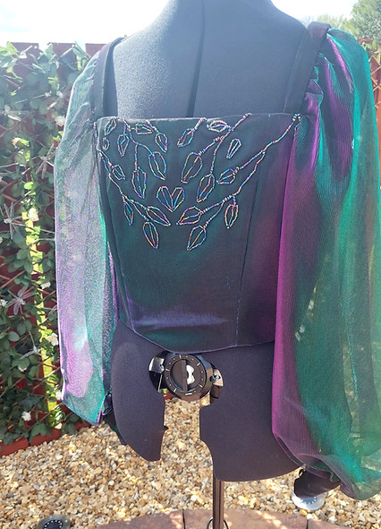 Long sleeved corset made with purple and green shifting fabric, decorated with beaded leaf details 
