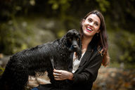 Femme brune tenant son chien noir dans les bras, sourires partagés