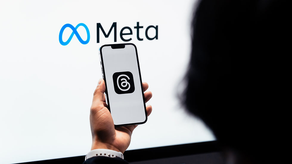 Hand holding a phone with the Threads logo in front of a Meta logo on a bright screen.
