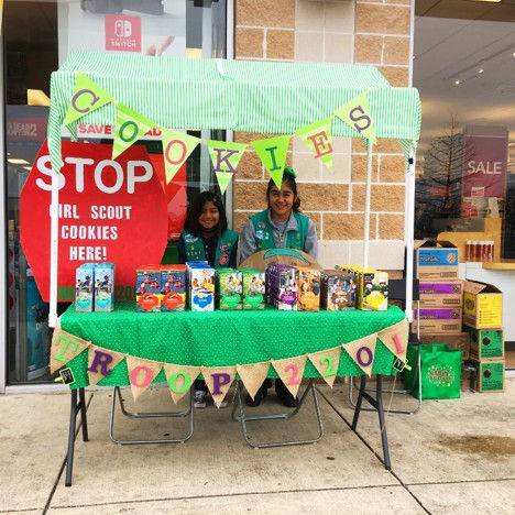 Girl Scouts selling cookies at a booth table