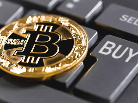 A bitcoin sitting on a keyboard with a key marked "BUY".
