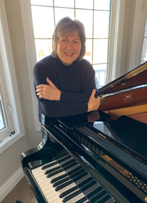 Susan leaning on piano in studio.