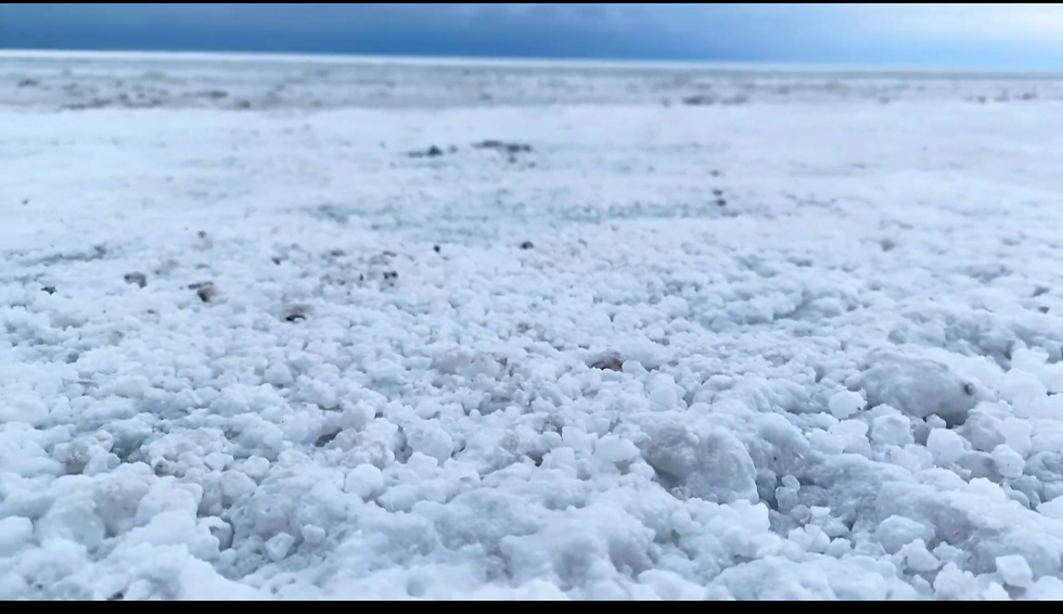 Close-up landscape photo of rough white salt crust on the ground stretching to the horizon under a blue sky, wide landscape aspect ratio.