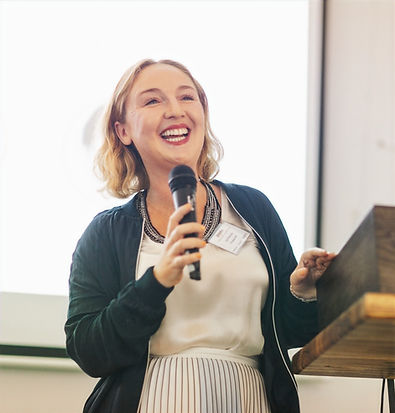 Founder Lisa Thomson onstage holding a microphone and speaking at an event