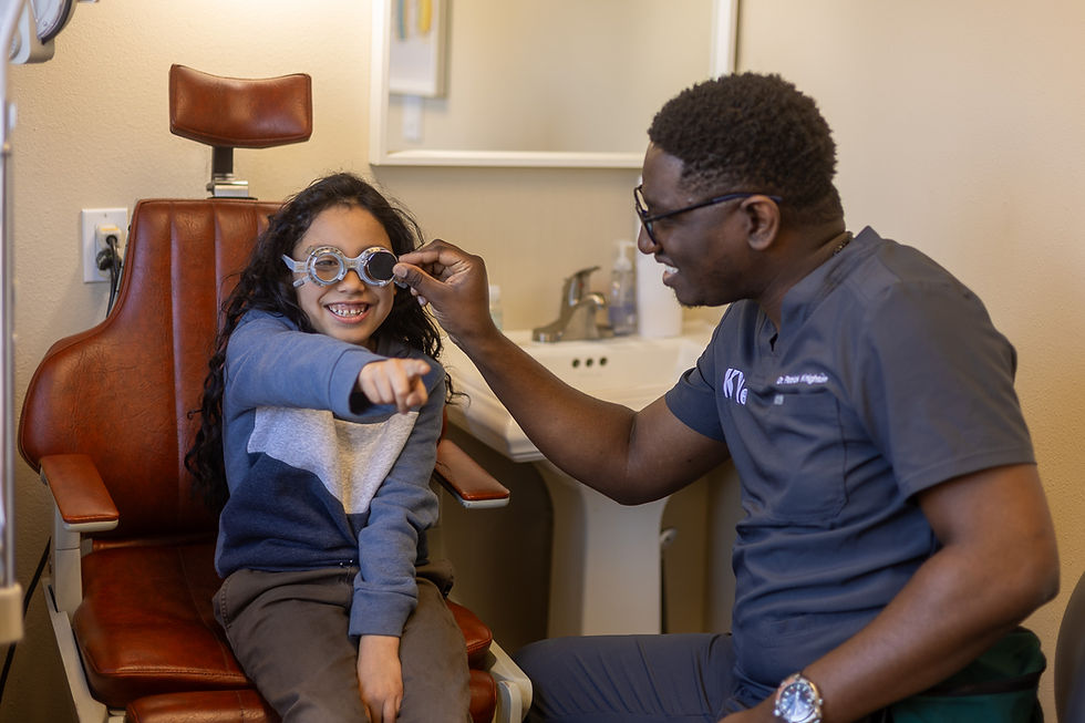 Smiling child tries on eye exam lenses as an optometrist adjusts them in a cozy clinic chair, with a sink and mirror behind them.