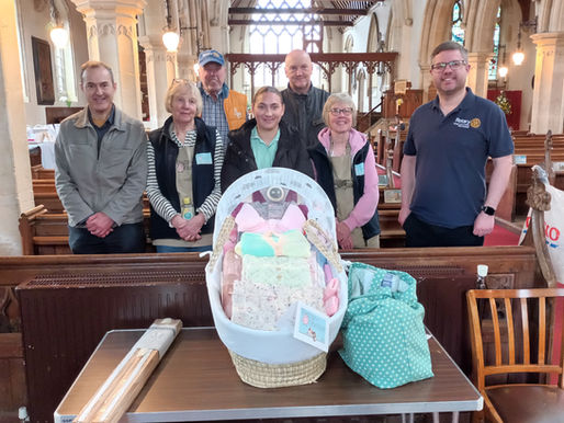 Pictured in St Nicholas Church Dersingham are (back row) Rotarians David Mills and Nigel Chettleburgh and (front Row) Rotary Satellite members Mark Collins (left) and Rob Colwell (right) with Maggie Anderson and Janet Kirk from Baby Basics. Kaitlyn (centre), Maternity Support Worker from the Rowan Midwife Hub, was there to collect and deliver the Moses basket pictured.