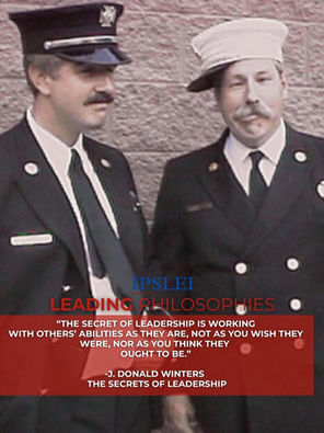 Older photo of two white firemen with moustaches, one is making a silly face and his hat is turned sideways.