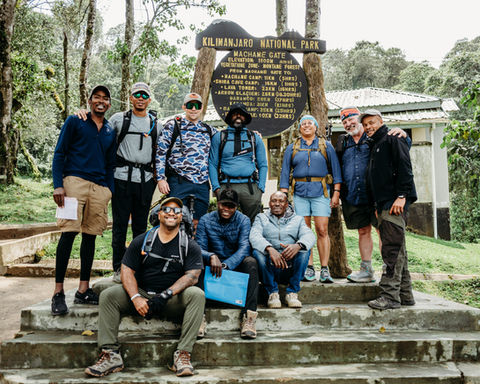 Group of hikers at Kilimanjaro National Park sign, Tanzania, ready for trek.