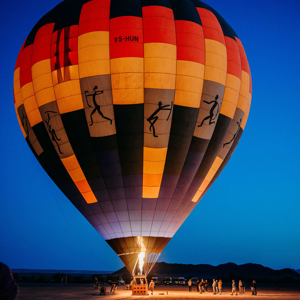 • Hot air balloon flying over the Namib Desert at sunrise.
• Namib Sky Balloon Safaris balloon lifting above the dunes.
• Balloon operator navigating over Namib-Naukluft National Park.
• Sunrise light over the sand dunes during a balloon ride.
• Aerial view of red sand dunes in the Namib Desert.
• Hot air balloon shadow cast on the desert floor.
• Couple inside the balloon basket during the flight.
• Balloon drifting above the rolling dunes of Namibia.
• Panoramic desert view from the hot air balloon.
• Balloon inflating before sunrise in the Namib Desert.
• Aerial landscape of the Namib-Naukluft at golden hour.
• Balloon pilot managing the burners during ascent.
• Scenic morning light across the Namib Desert.
• Hot air balloon landing area in the desert.
• Peaceful desert horizon viewed from the balloon basket.