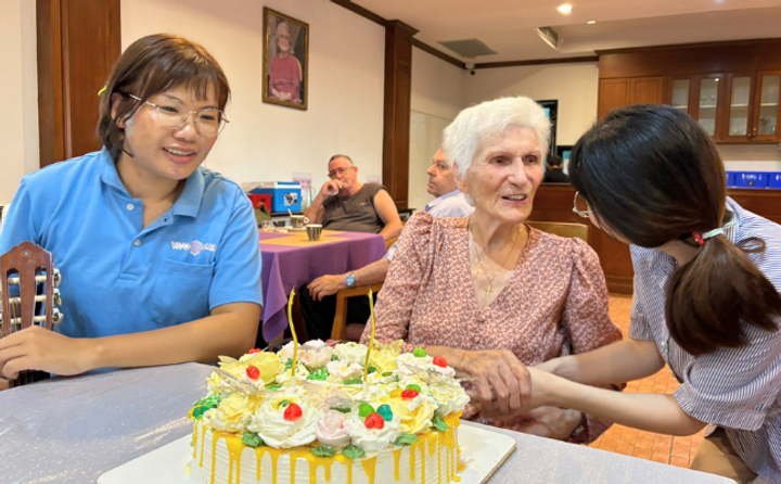 Elderly woman celebrating her birthday at VivoCare, surrounded by caregivers and a festive cake.