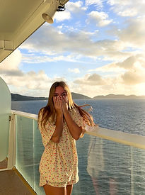 Girl on balcony of cruise ship looking at island ahead