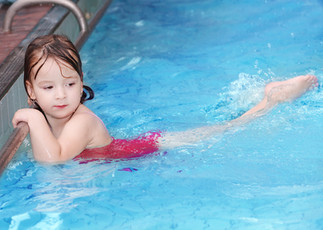 A child at the edge of the pool practicing swim kicks
