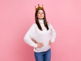 Femme portant une couronne en carton sur fond rose, illustrant le masque du narcissisme et la fausse confiance en soi