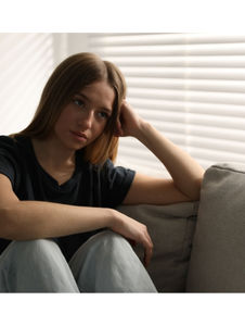 Adolescente assise sur un canapé le regard triste, illustrant le mal-être adolescent et le besoin d'un accompagnement thérapeutique à domicile