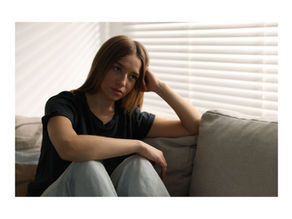 Adolescente assise sur un canapé le regard triste, illustrant le mal-être adolescent et le besoin d'un accompagnement thérapeutique à domicile