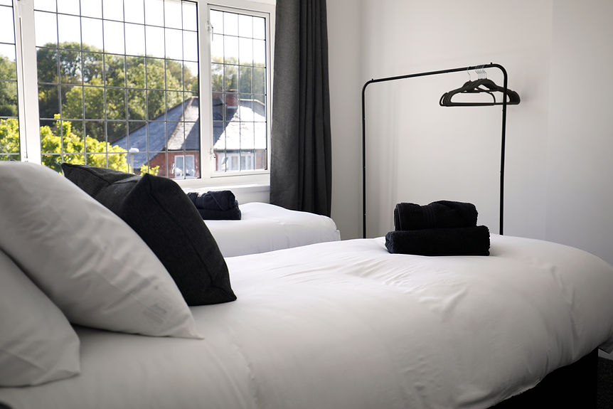 Two beds with white bedding, black pillows, a window overlooking trees.