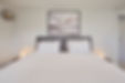 Bedroom with a white bed, dark headboard, and abstract artwork