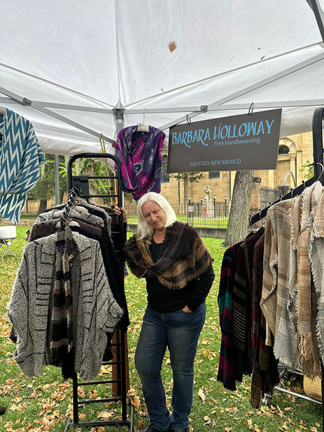 Fiber artist Barbara Holloway presenting handwoven garments at 2025 Cathedral Park Santa Fe show.