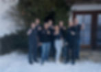 Das SPS-Team in Freizeitkleidung steht lächelnd vor einem verschneiten Gebäude mit großen Fenstern. Efeu bedeckt einen Teil der Wand und schafft eine gemütliche Atmosphäre.