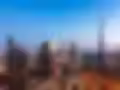 Skyline of a city at dusk with modern skyscrapers, including a tall, prominent tower. The streets are brightly lit, conveying a vibrant, urban atmosphere.