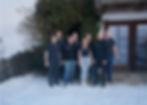 Das SPS-Team in Freizeitkleidung steht lächelnd vor einem verschneiten Gebäude mit großen Fenstern. Efeu bedeckt einen Teil der Wand und schafft eine gemütliche Atmosphäre.