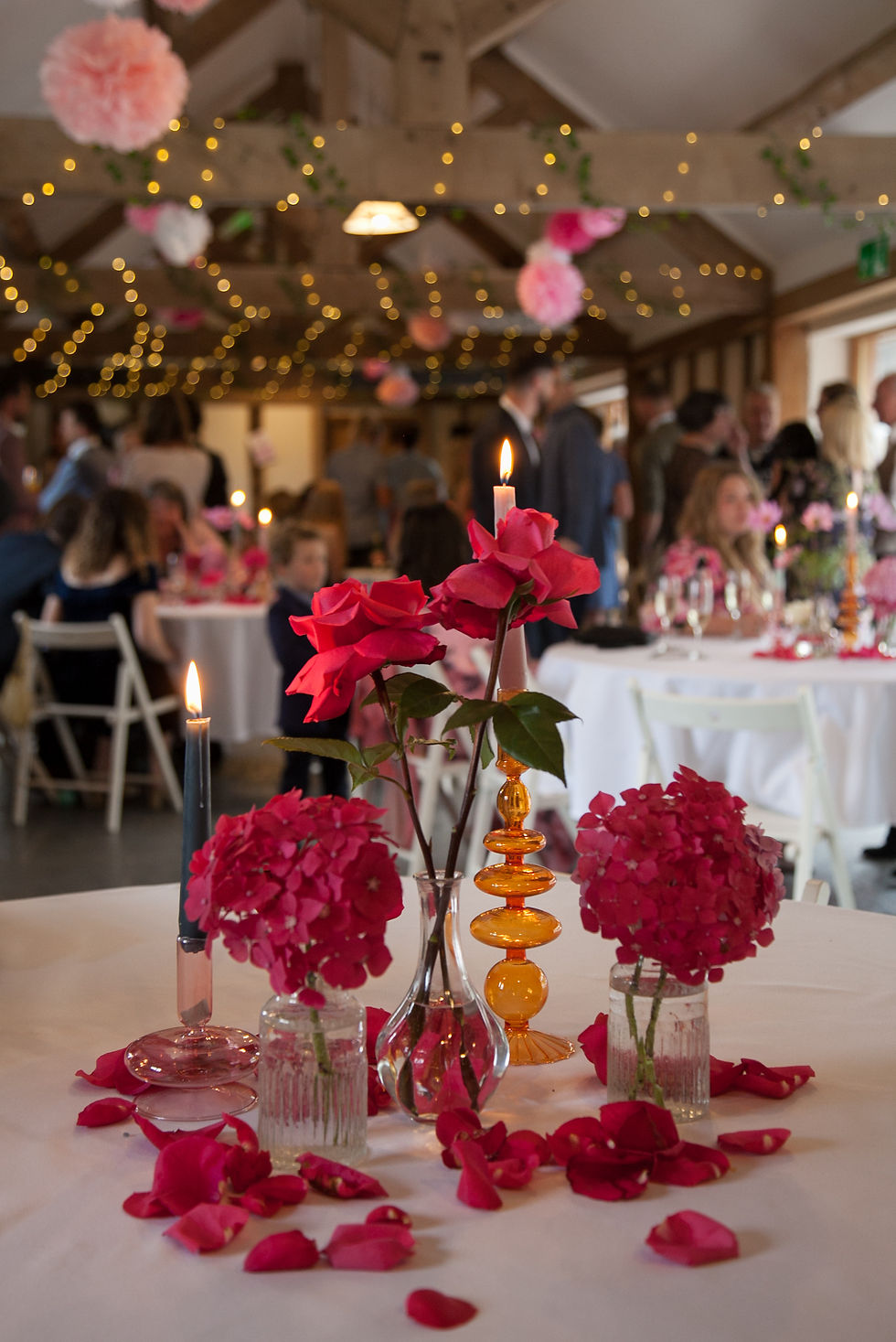 Wedding tablescape with pink and orange glass candleholders, scattered rose petals and bud vases with single stem pink hydrangeas and pink roses.