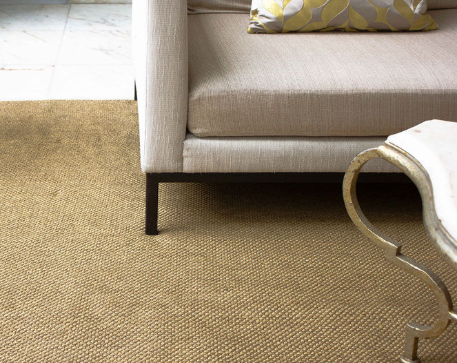 Close-up of a tan woven area rug positioned under a beige sofa and a marble coffee table with curved brass legs.