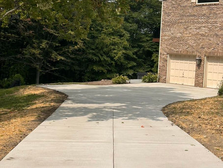 Newly installed concrete driveway leading to a brick home, surrounded by trees and landscaping in early fall.