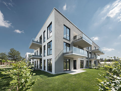 Modernes Mehrfamilienhaus mit Balkonen und Gartenfläche, helle Putzfassade.