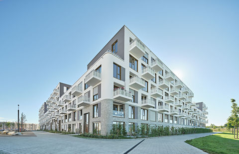 Eckansicht eines modernen Wohngebäudes mit Balkonen und strukturierter heller Fassade.