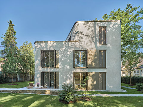 Modernes, kubisches Wohnhaus mit Flachdach und großen Fenstern inmitten einer grünen Rasenfläche.