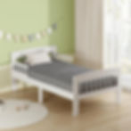 A white wooden toddler bed frame with a grey chevron mattress positioned against a soft green nursery wall.