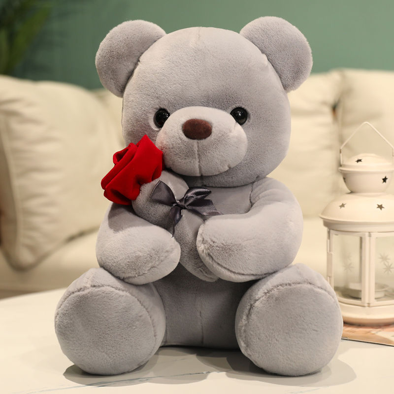 A cute grey stuffed teddy bear holding a red plush rose.