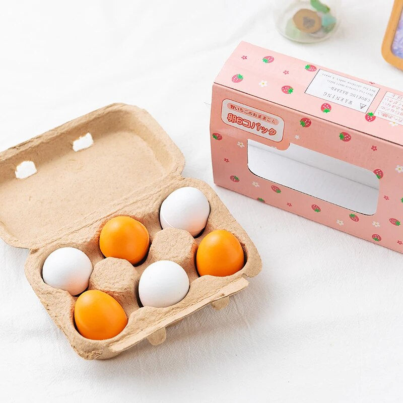 Six wooden play eggs sitting in an open carton next to a cute pink retail box decorated with strawberries and Japanese text.